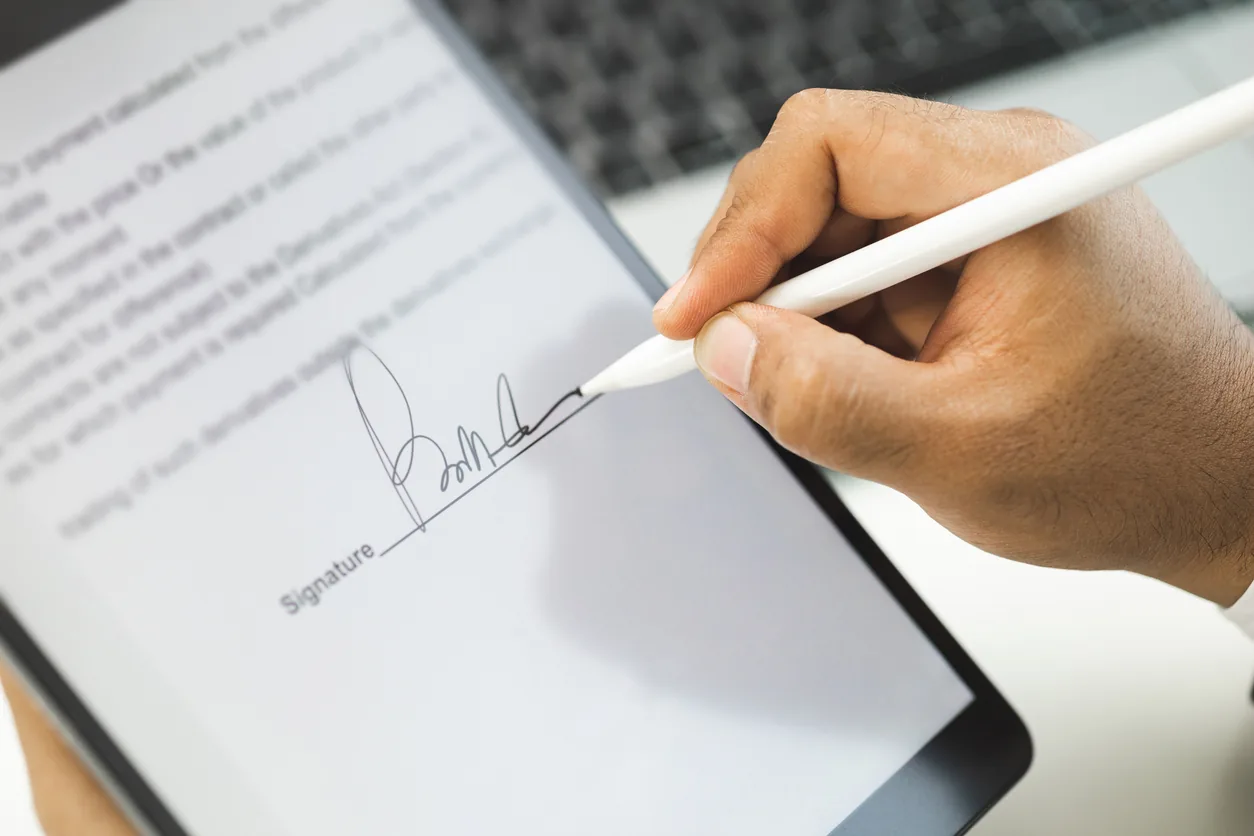 A hand signing a document with a digital signature on a tablet
