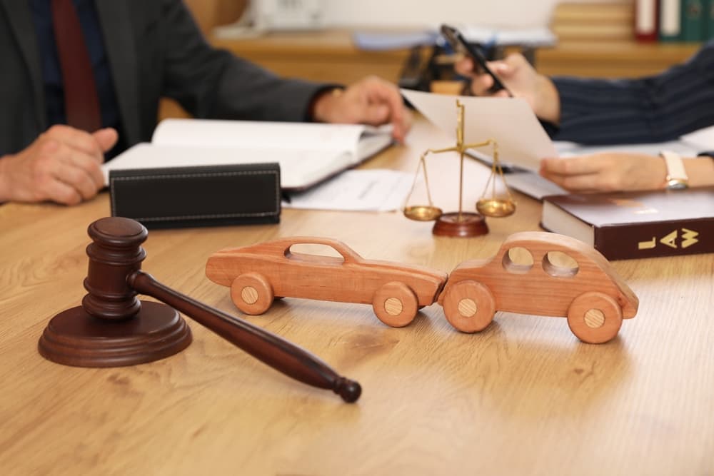 Car accident lawyer discussing case with client with two wooden car models and gavel on the table
