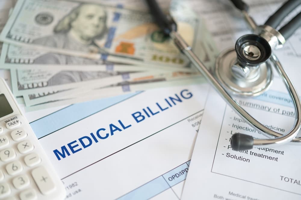 Medical billing document and dollar banknote, calculator, stethoscope.