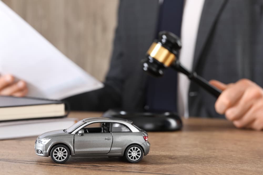 Auto accident law. Man with document and gavel at wooden table indoors, focus on toy car